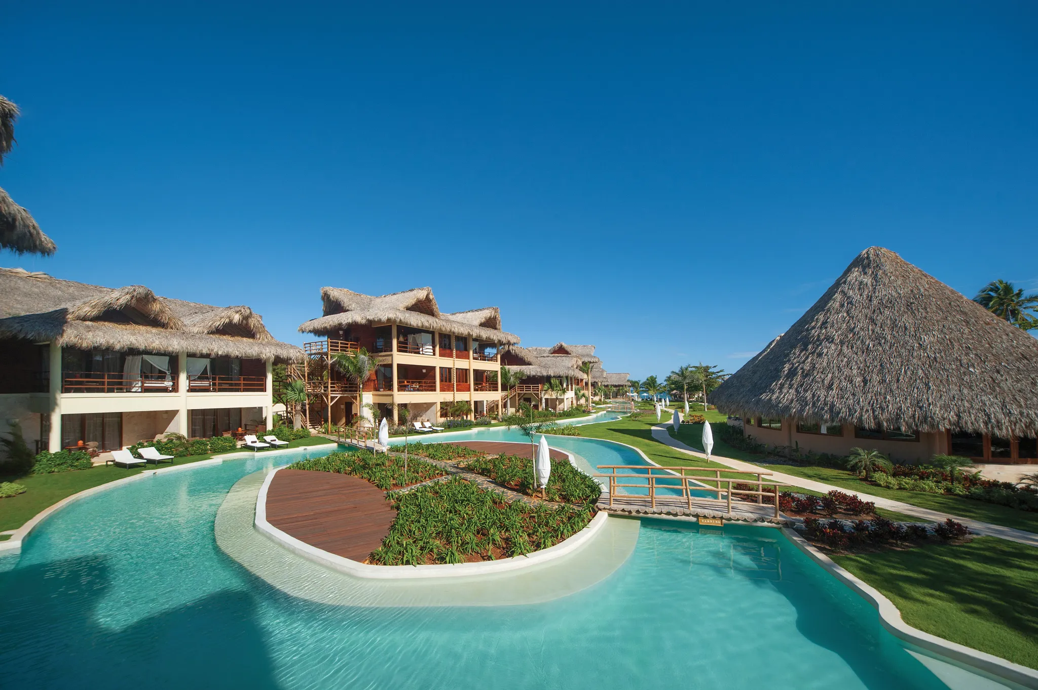 Expansive lagoon pool surrounded by thatched-roof suites at Zoëtry Agua Punta Cana.