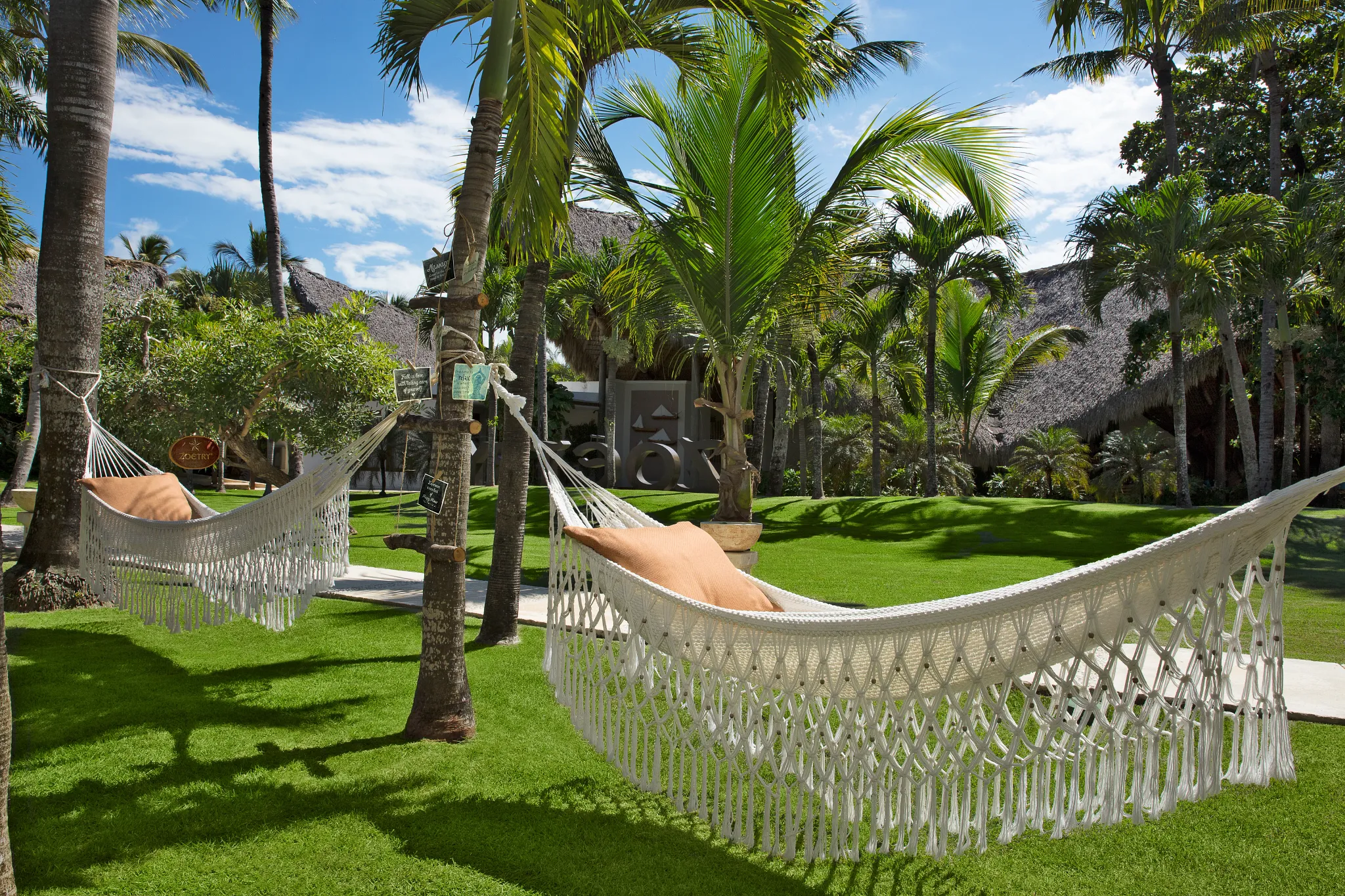 White hammocks hanging between palm trees in the tropical gardens of Zoëtry Agua Punta Cana.